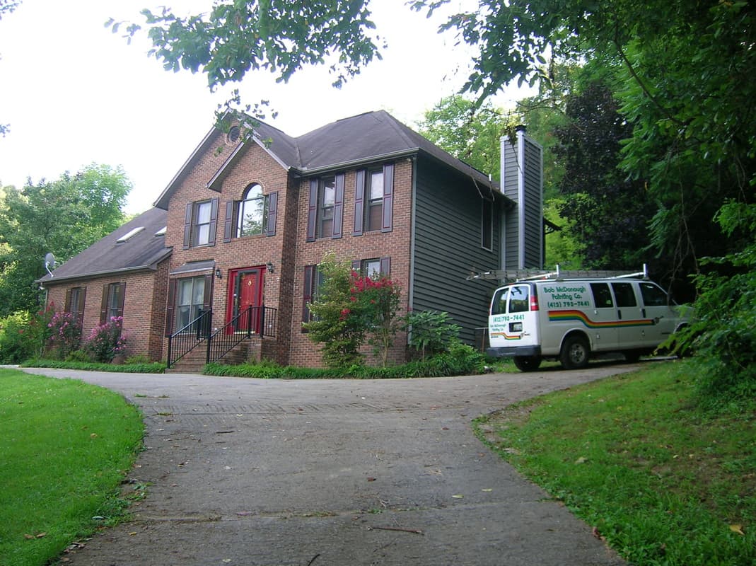 A well painted brick home with the Bob McDonough Painting company van parked in front.